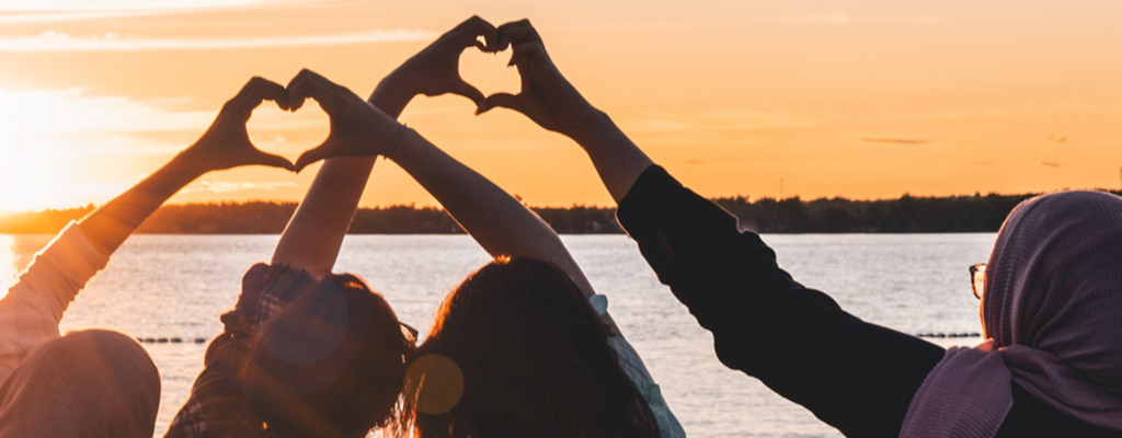 Four people making heart shaped silhouettes with their joined hands against a sunset backdrop